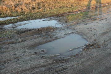 two big puddle of  gray dirty water on the brown earth of the road