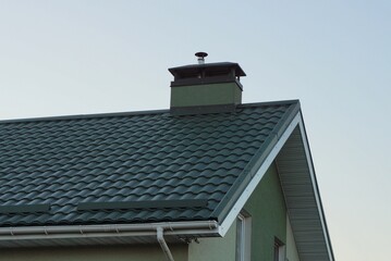 part of the roof of a private house under green tiles with a concrete chimney against a gray sky