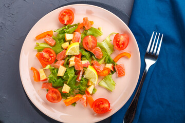 Salad with salmon and cherry tomatoes on a concrete background on a blue napkin next to a fork.