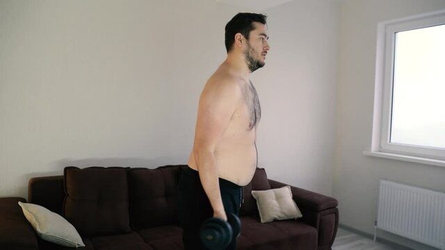 fat man lifting dumbbell weights sitting at home. weight loss concept. home fitness