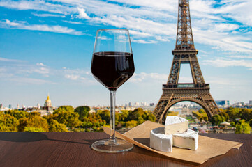Glass of wine with brie cheese on Eiffel tower and Paris skyline background. Sunny view of glass of red wine overlooking the Eiffel Tower in Paris, France - obrazy, fototapety, plakaty