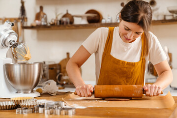 Caucasian focused pastry chef woman making dough at cozy kitchen