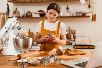 Smiling pastry chef woman using mobile phone while cooking cake