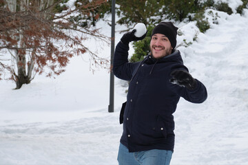 Fototapeta na wymiar Young caucasian man ready to throw a snowball in a park during Filomena snowstorm in Madrid, Spain. Winter activities.