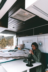 Image of a young brunette, having lunch and coffee, inside a camper, in the winter