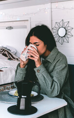 Image of a young brunette, having lunch and coffee, inside a camper, in the winter