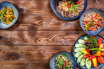 Flat layout of various dishes with sliced vegetables, meat cuts, salads on a brown wooden background. Copy space.