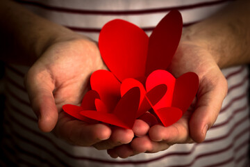 Valentine's Day background. Red paper hearts are laid out on the palms of a man. Bright colorful hearts for a gift to a loved one. - 404883538