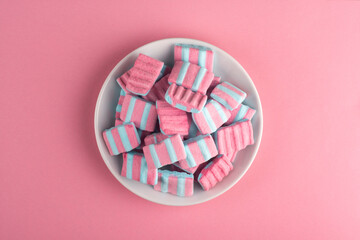 Pink marshmallows in a plate on a pink background.