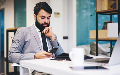 Thoughtful entrepreneur using smartphone in workspace