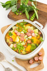 Vegetable soup with sausages in a soup tureen with pea pod and spoon