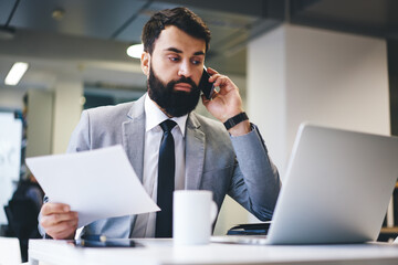 Serious entrepreneur speaking on smartphone in office