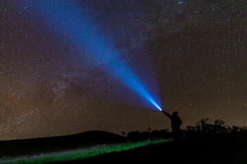 Climber or backpacker. Light holds up over his head. Standing on mountain peak. man with flashlight point to the starry sky at midnight. tourist with flashlight