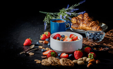 Fototapeta na wymiar Traditional healthy breakfast foods and drinks - oats, granola, yoghurt, toasts, cereal, croissants, with fruit, berry and coffee on dark background. Diet food or healthy food in the morning