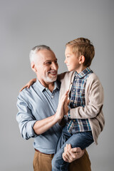 smiling grandfather giving high five to grandson while holding him isolated on grey