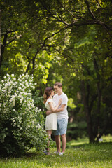 Naklejka na ściany i meble Young man and woman couple in a blooming garden near jasmine bush. Tender holding each other. Spring love story. Brown-haired girl with long hairs with her boyfriend or husband. Young couple on a date