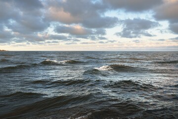 Panoramic view of the open Baltic sea at sunset. Dramatic sky with colorful glowing cumulus clouds. Water surface texture close-up. Fickle weather, winter, climate change, ocean swell, nature - 404890925