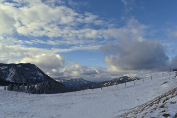 	
Schneelandschaft mit verschneiten verkrüppelten Bäumen im Gebirge vor blauem Himmel mit Wolken	
