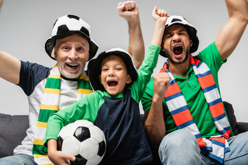 happy men and boy in fan hats shouting and showing win gesture while watching football match isolated on grey