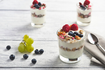 natural yogurt with raspberries and blueberries  in a glass on a white wooden background, clean and airy look