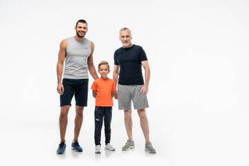happy boy with dad and grandfather in sportswear looking at camera on white