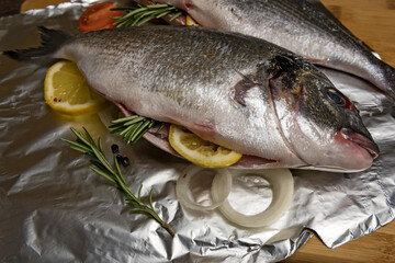 Fresh dorado fish. Stuffing fish with lemon, rosemary and other ingredients. On the foil, a wooden table and a wooden Board.