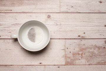 Empty white mug cup with a tea bag in it waiting to be brewed with hot water on a texture white wooden table surface with copy space and room for text