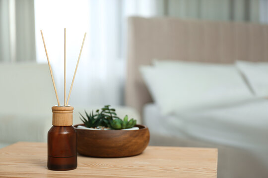 Air reed freshener and houseplants on wooden table in bedroom. Space for text