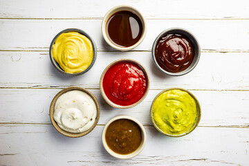 Set of different bowls of various dip sauces on white background, top view