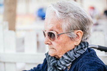 Elderly caucasian woman with pink sunglasses sitting on a wheelchair in a bar