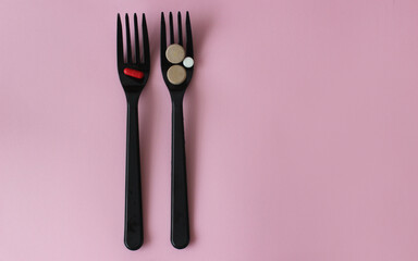 Two black plastic forks with colored tablets on a pink background.