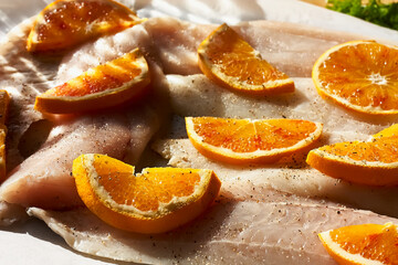 Cod fish fillet with oranges on baking paper. Seafood, healthy eating. Natural light. Selective focus.