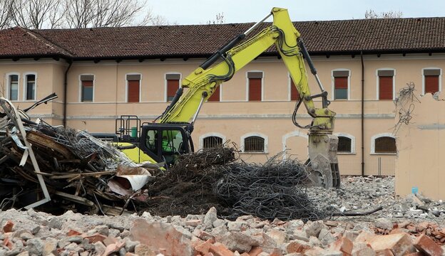 Yellow excavator, among debris and scrap metal,  demolishes a building during an urban redevelopment.