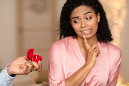 Black man making proposal with ring, confused woman rejecting