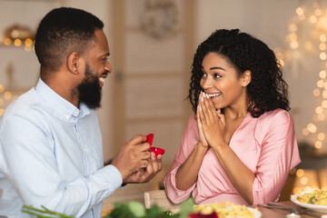 Smiling afro guy making proposal with ring to his fiance - obrazy, fototapety, plakaty