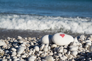 Red heart painted with a red paint marker on the pebble as a gift for Saint Valentine's day on the sea 
 background. Spontaneous symbol of love and passion. 