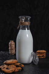 Bottle of fresh milk and chocolate homemade cookies served on table in dark studio on black background 