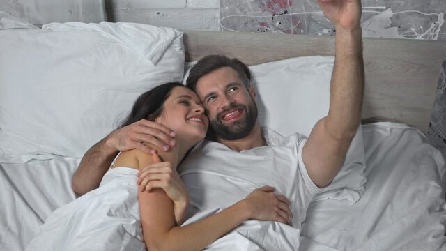 cheerful couple lying on bed and taking selfie