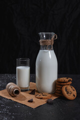 Glass and bottle of tasty milk and stack of chocolate chip cookies arranged on dark table for rustic healthy breakfast on black background in studio 