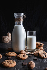 Bottle and glass of fresh milk on table with cookies and chocolate on black background in studio 