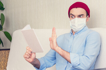 Alarmed guy in a medical mask holds book and show sign stop, portrait, toned