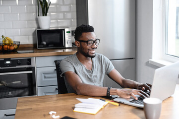 Happy smiling business man distantly working from home. Successful male freelancer sitting at the desk, using laptop, develop a project. African american student on a lecture, online study concept