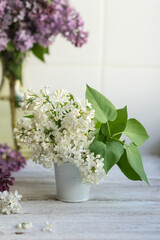 Bouquet of white spring flowers of lilac in a ceramic vase on a light background of kitchen tiles. Festive interior decoration