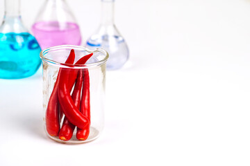 Red chili in a glass, a blurred science test tube in the background.Chili Extract Concept.	
