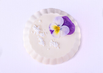 Fototapeta na wymiar Panna cotta of white cocolate and wipped cream decorated with edible violet flower over on white background.Top view. Overhead. Copy space.
