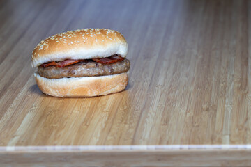 Simple burguer with bacon standing on a wooden table.