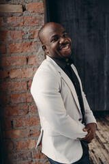 Obraz premium African American man posing at camera, smiling, leaning against wall in loft studio.Style and business concept