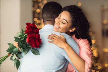 Smiling young black woman hugging man holding red roses