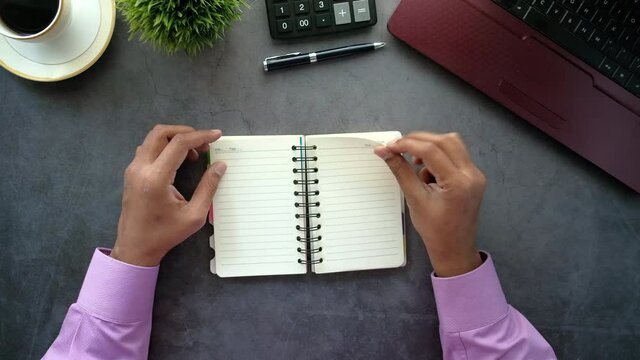 top view of man's hand turning a pager of a notepad with laptop on table 