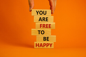 You are free to be happy symbol. Male hand. Wooden blocks tower with words 'You are free to be happy'. Beautiful orange background. Copy space. Business and motivational concept.